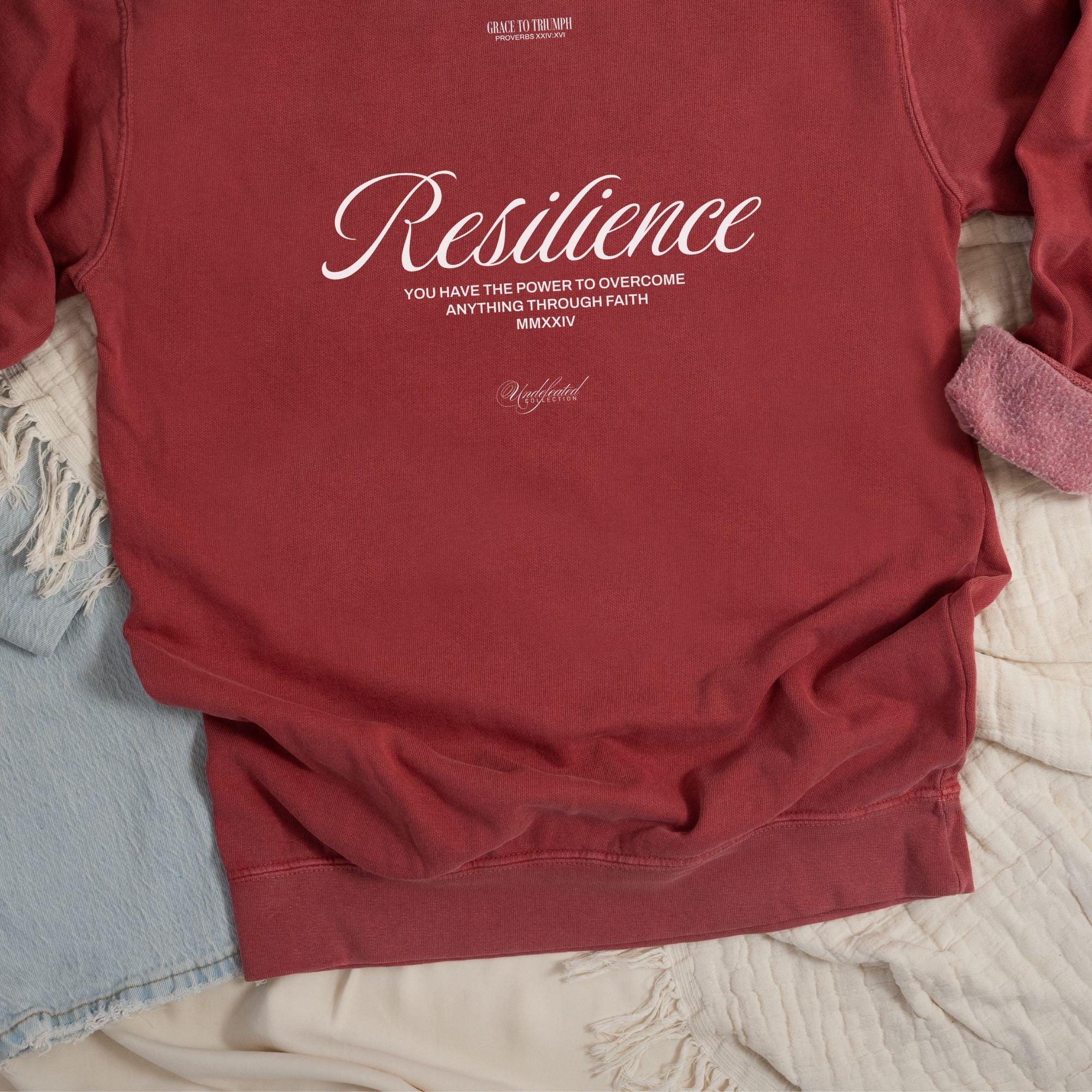 A Flat lay mockup of back design of crimson color sweatshirt with text design that partly reads "Resilience - Undefeated"