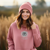 model wearing a dusty rose hoodie with design that features a bible verse that says 'Romans 828, It's All Good' in white and black embroidery